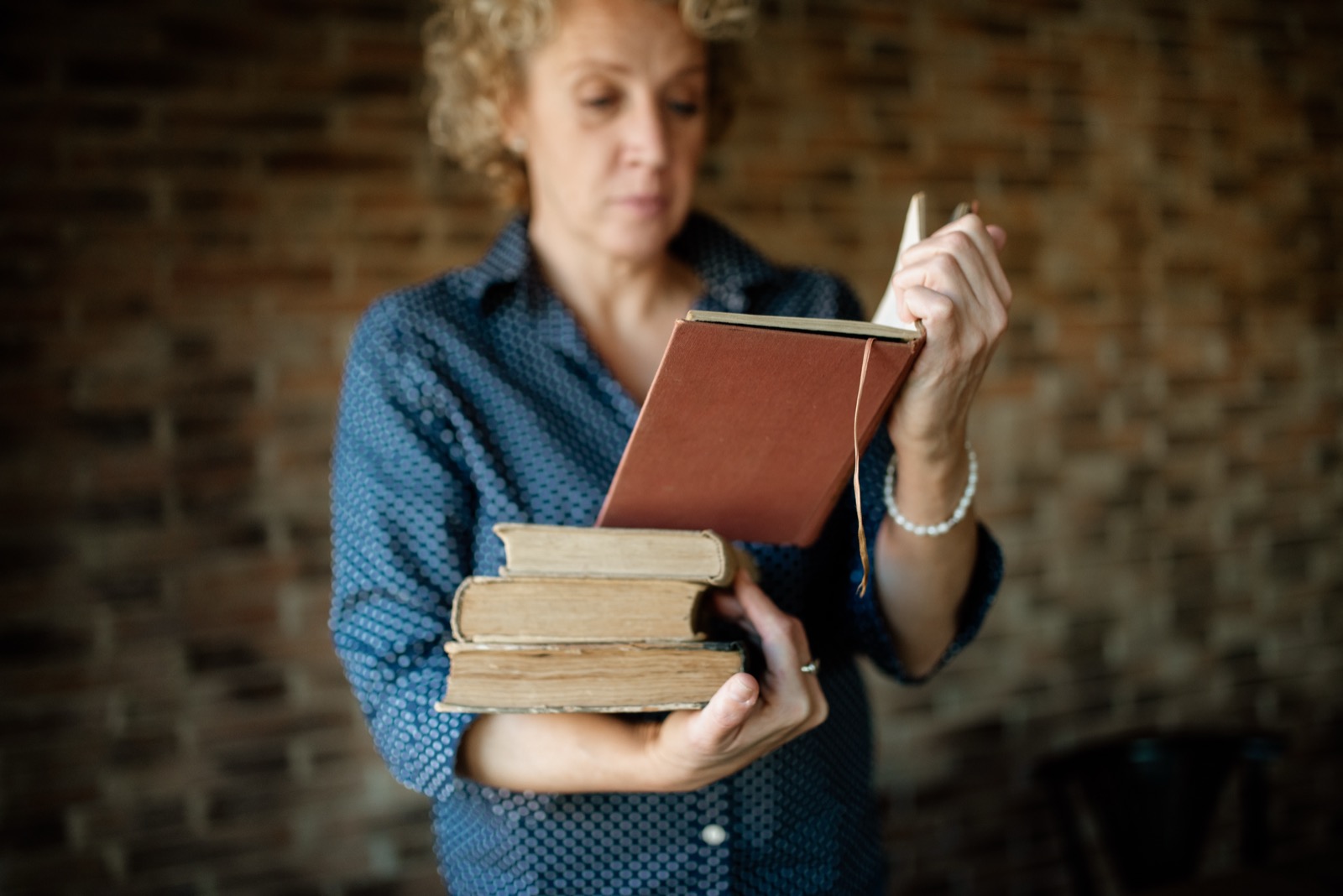 A woman holding a stack of older books while looking at the top volume