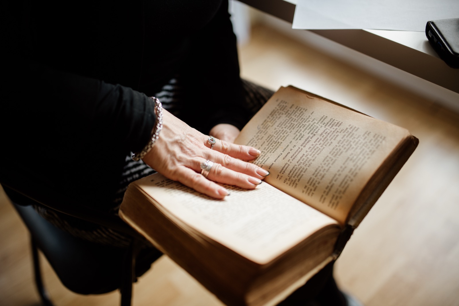 A reader’s hands resting on the pages of an open older book beside a window