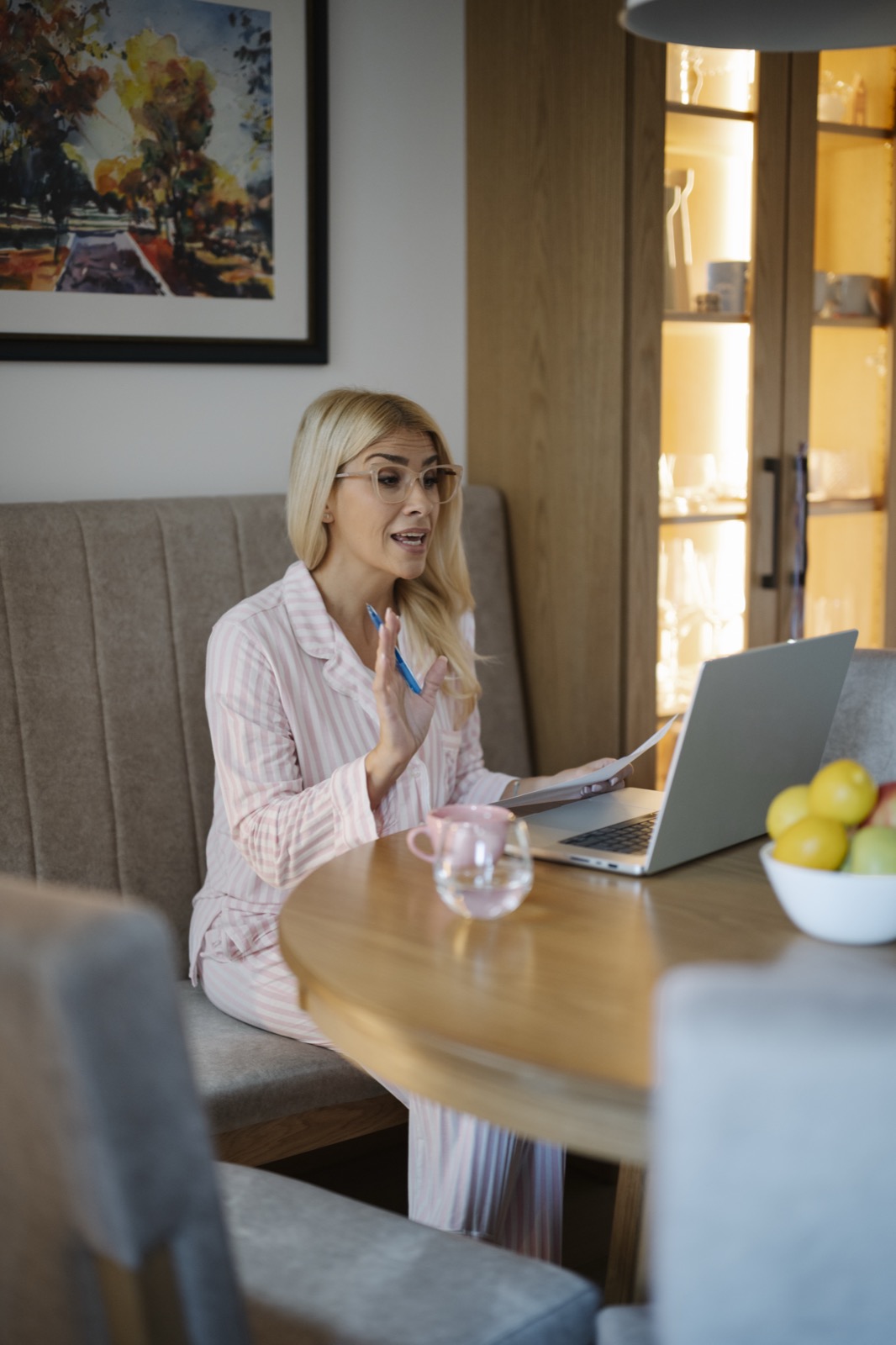 A woman seated at a table speaking beside papers and an open laptop
