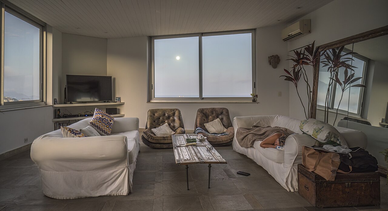 An everyday living room with chairs, sofas, a table, and evening window light