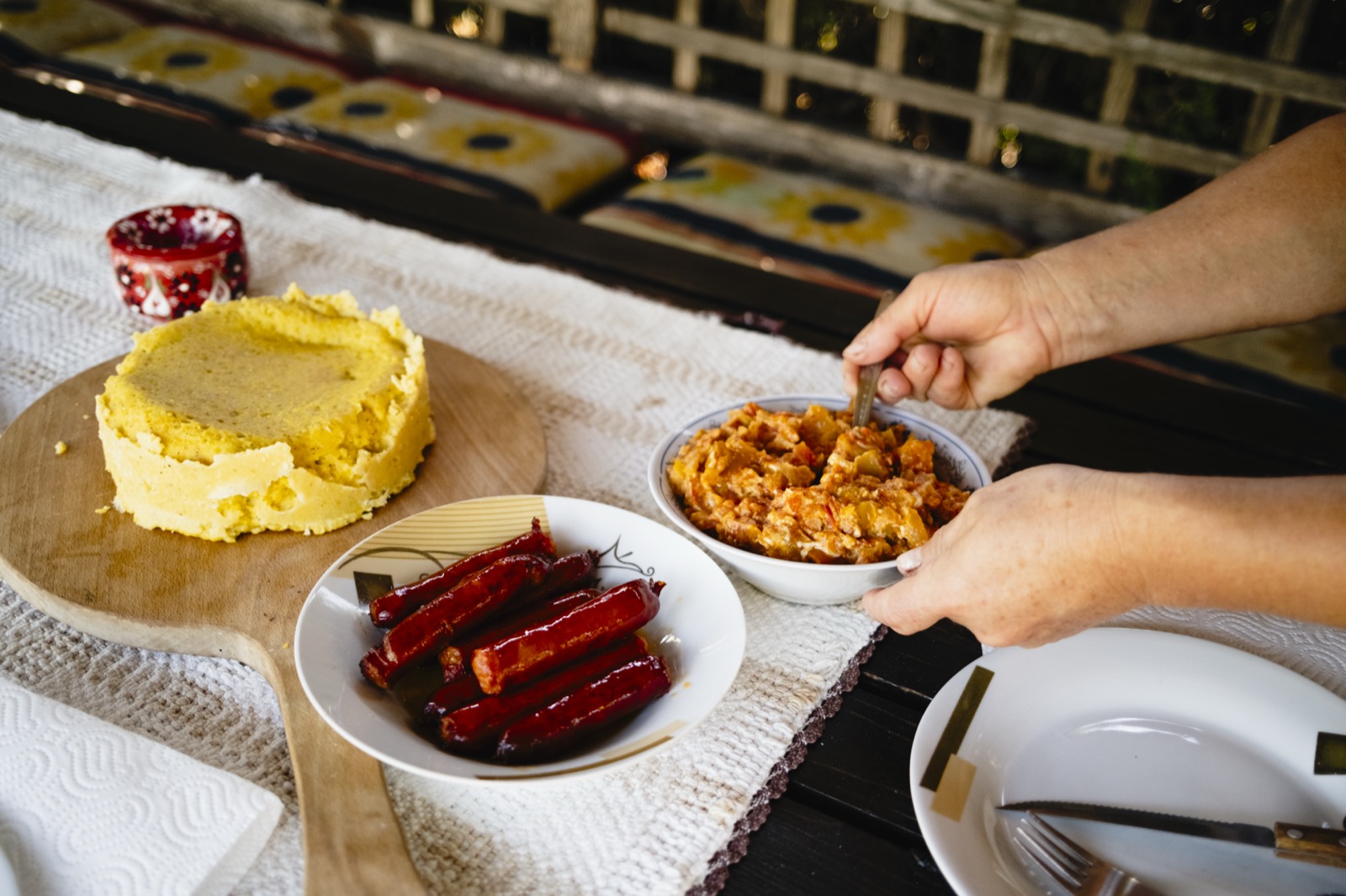 Hands serving from a bowl beside polenta and sausages on a table