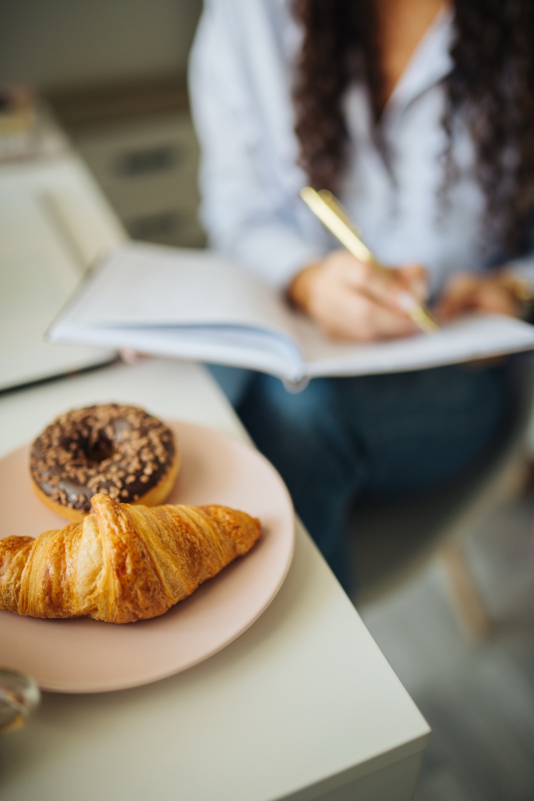A person writing in an open notebook at a table with breakfast pastries