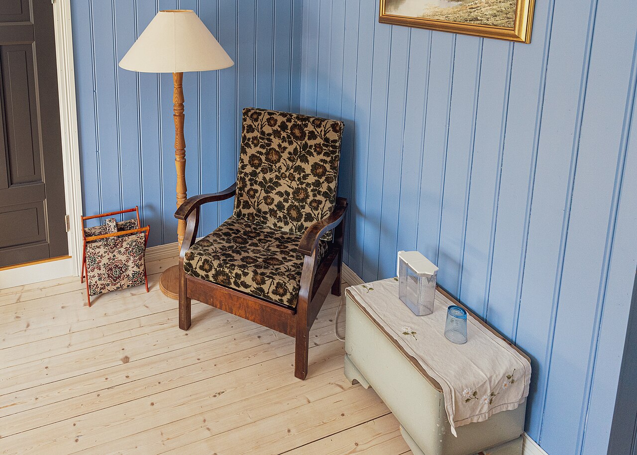 A reading corner with an armchair, lamp, and a book on a nearby chest