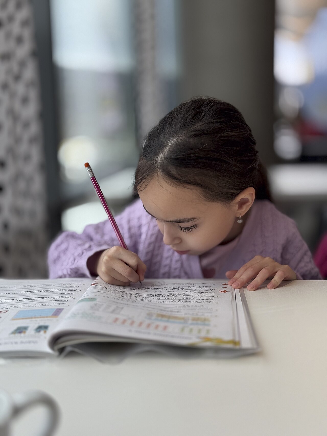A child working in a notebook at a table in a bright room