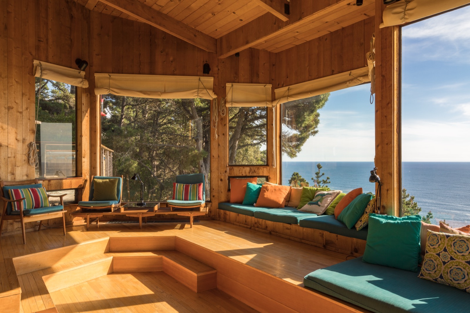A living room with broad windows and seating arranged beside the outdoor view