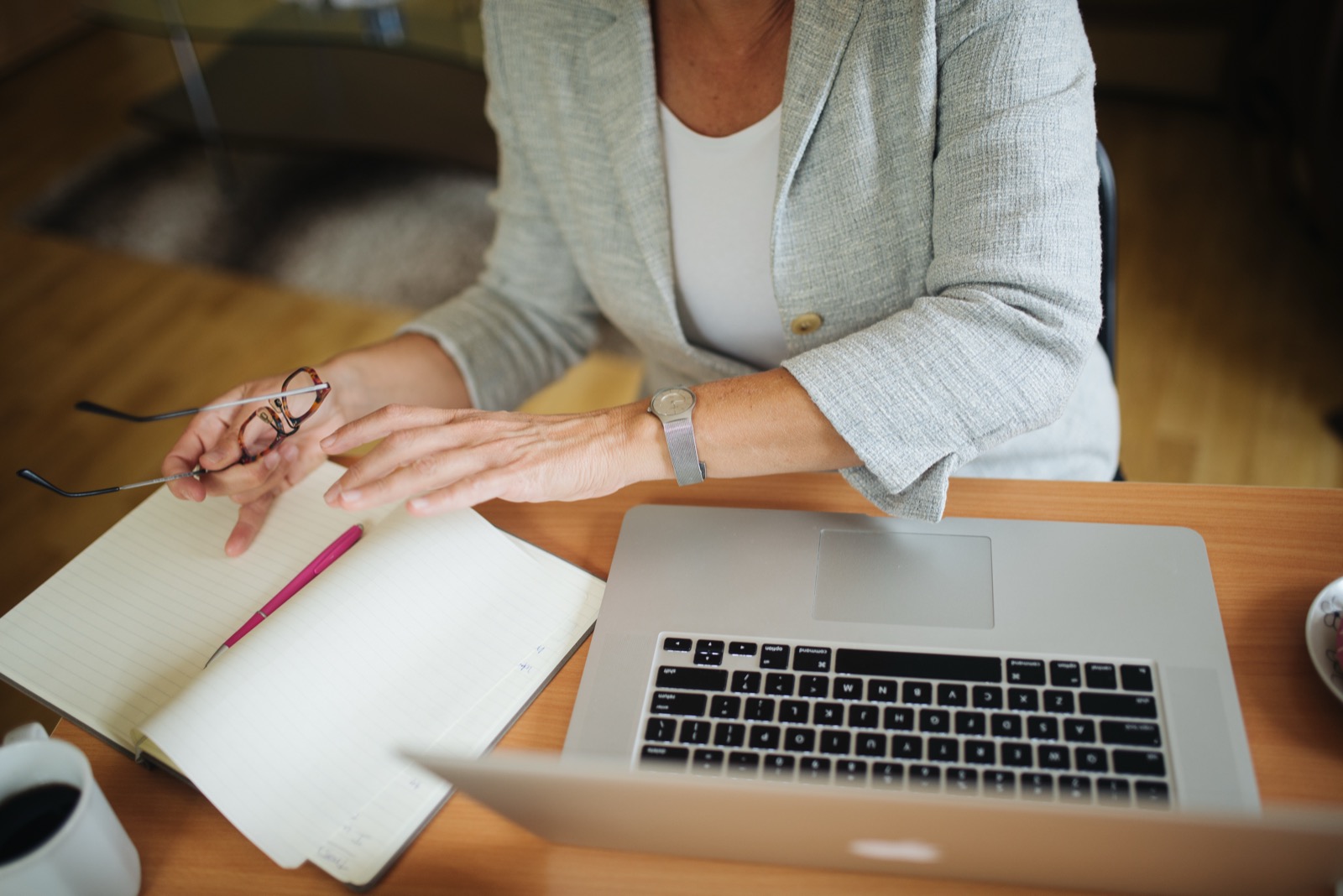 A woman seated at a desk looking over an open lined notebook beside a laptop